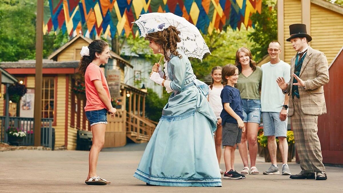 A woman in 1800s dress talking with a young girl while her family waits in the background at Silver Dollar City